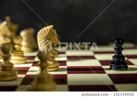 Closeup view of a white chess knight standing against the opposing pieces on the chessboard. Concept of strategy Closeup view of a white chess knight standing against the opposing pieces on the chessboard. Concept of strategy 132334058