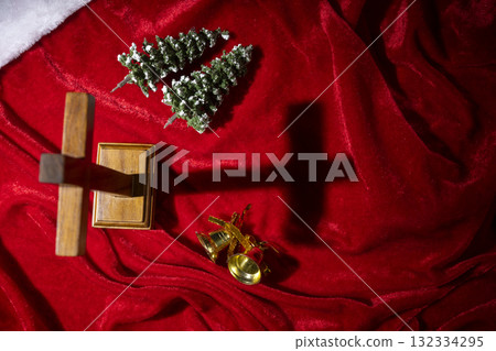 Christian cross with miniature Christmas trees and golden bells on a red silk background. Concept of faith, holiday celebration, and spiritual reflection Christian cross with miniature Christmas trees and golden bells on a red silk background. Concept of faith, holiday celebration, and spiritual reflection 132334295