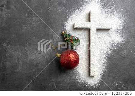 Christian cross with a dusting of white powder and a miniature Christmas tree with Christmas ball ornaments on the table. Concept of faith, holiday celebration, and spiritual reflection Christian cross with a dusting of white powder and a miniature Christmas tree with Christmas ball ornaments on the table. Concept of faith, holiday celebration, and spiritual reflection 132334296