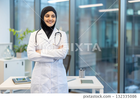 Muslim female doctor in a hijab and lab coat, confidently standing with arms crossed in a modern office, smiling and exuding professionalism in healthcare Muslim female doctor in a hijab and lab coat, confidently standing with arms crossed in a modern office, smiling and exuding professionalism in healthcare 132335086