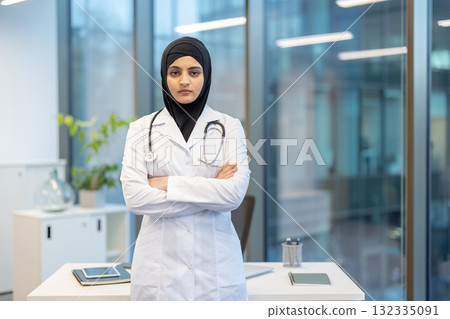 Muslim woman doctor wearing a hijab and white lab coat, standing with arms crossed in a modern office, representing professionalism and dedication in healthcare Muslim woman doctor wearing a hijab and white lab coat, standing with arms crossed in a modern office, representing professionalism and dedication in healthcare 132335091