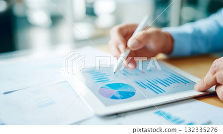 Hands using a stylus on a tablet with data visualizations, emphasizing remote work efficiency in a contemporary home office setting Hands using a stylus on a tablet with data visualizations, emphasizing remote work efficiency in a contemporary home office setting 132335276
