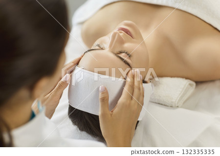 Esthetician performing facial massage for woman client in bright spa treatment room Esthetician performing facial massage for woman client in bright spa treatment room 132335335