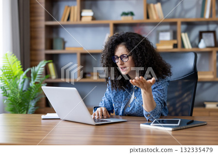 Young woman working from home having a video call on her laptop is getting frustrated and arguing with a client or colleague, gesturing with her hand Young woman working from home having a video call on her laptop is getting frustrated and arguing with a client or colleague, gesturing with her hand 132335479