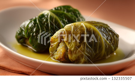 Stuffed Cabbage Rolls Glazed with Broth on White Plate Against Warm Background 132335507