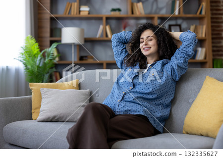 Young woman enjoying a moment of peace and relaxation on her comfortable sofa, hands behind her head, eyes closed, a peaceful smile on her face, surrounded by the cozy atmosphere of her living room Young woman enjoying a moment of peace and relaxation on her comfortable sofa, hands behind her head, eyes closed, a peaceful smile on her face, surrounded by the cozy atmosphere of her living room 132335627