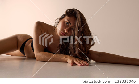 Woman lying on floor in black lingerie under warm light for beauty, fashion, and lifestyle ads 132336040