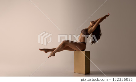 Woman leaning back on wooden block in brown lingerie under warm light 132336055