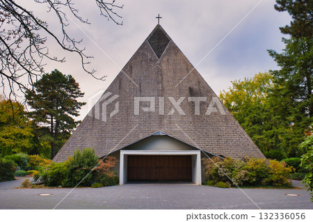 Triangular Pyramid-Shaped Church Building with Cross Top Surrounded by Lush Autumn Foliage and Overcast Sky in Serene Park Setting Triangular Pyramid-Shaped Church Building with Cross Top Surrounded by Lush Autumn Foliage and Overcast Sky in Serene Park Setting 132336056