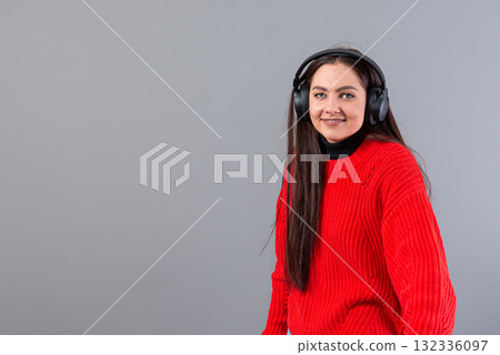 positive girl brunette in red sweater listens to music on smartphone in headphones, isolated on gray positive girl brunette in red sweater listens to music on smartphone in headphones, isolated on gray 132336097