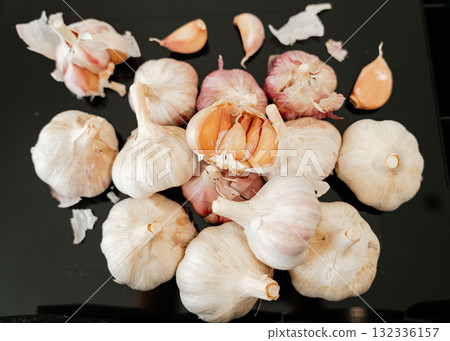 Bunch of garlic bulbs and cloves scattered on glossy black table reflection and organic food concept Bunch of garlic bulbs and cloves scattered on glossy black table reflection and organic food concept 132336157