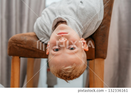 Boy hanging upside down from a chair, smiling playfully candid indoor portrait full of fun and energy 132336161