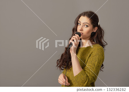 attractive teenager woman speaking with a microphone against gray background, conference speaker attractive teenager woman speaking with a microphone against gray background, conference speaker 132336282