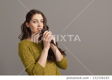 attractive teenager woman speaking with a microphone against gray background, conference speaker attractive teenager woman speaking with a microphone against gray background, conference speaker 132336283