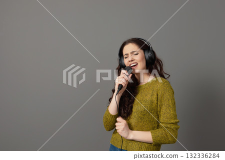cheerful young woman in casual clothes with headphones sing song in microphone, mock up copy space cheerful young woman in casual clothes with headphones sing song in microphone, mock up copy space 132336284