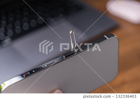 Modern mobile phone with a SIM card ejector tool inserted into its tray slot, crucial for activating network services and establishing global digital connectivity Modern mobile phone with a SIM card ejector tool inserted into its tray slot, crucial for activating network services and establishing global digital connectivity 132336401