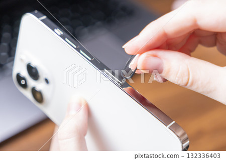 Woman's hand carefully inserts a SIM ejector tool into a modern smartphone to open the card slot, enabling essential mobile network connectivity Woman's hand carefully inserts a SIM ejector tool into a modern smartphone to open the card slot, enabling essential mobile network connectivity 132336403