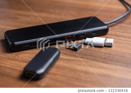 Sleek black USB-C multi-port docking station with HDMI, USB ports, and additional adapters, providing extensive connectivity for modern digital devices on a wooden desk 132336416