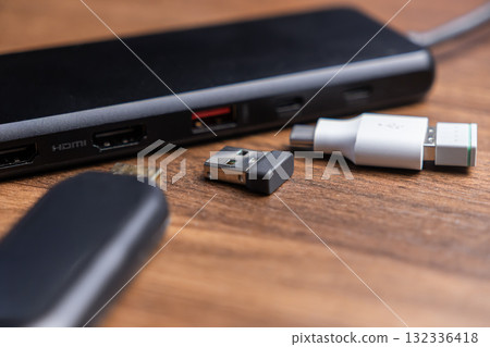 Black USB-C multiport hub, HDMI port, wireless dongle, and USB-C adapter on wooden desk, providing expanded connectivity for modern devices Black USB-C multiport hub, HDMI port, wireless dongle, and USB-C adapter on wooden desk, providing expanded connectivity for modern devices 132336418