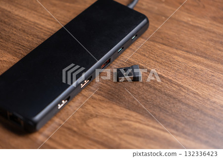 Black USB hub with multiple ports, positioned beside a tiny wireless dongle, essential for expanding modern digital workspace connectivity and device peripherals Black USB hub with multiple ports, positioned beside a tiny wireless dongle, essential for expanding modern digital workspace connectivity and device peripherals 132336423