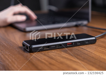 Black multi-port USB-C hub connected to a rich wooden desk, expanding versatile connectivity for modern digital productivity 132336425