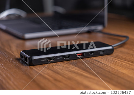 Black USB-C hub with multiple HDMI, USB, and PD ports connected to a laptop on a wooden desk, optimizing modern digital workspace connectivity for productivity 132336427