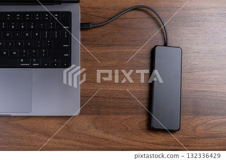 Modern laptop connected to a black external drive on a wooden desk, symbolizing crucial data backup, digital storage, and portable file management 132336429