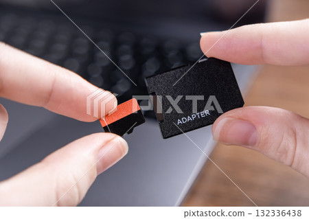 Human hands holding a small micro SD card and an ADAPTER, preparing for data transfer with a laptop, representing digital storage Human hands holding a small micro SD card and an ADAPTER, preparing for data transfer with a laptop, representing digital storage 132336438