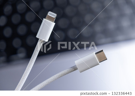 Modern white braided cables displaying Lightning and USB-C connectors, highlighting universal connectivity and compatibility for rapid device charging and efficient data transfer Modern white braided cables displaying Lightning and USB-C connectors, highlighting universal connectivity and compatibility for rapid device charging and efficient data transfer 132336443