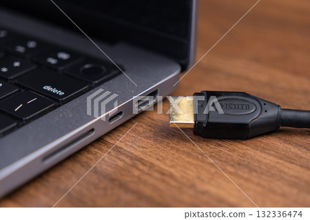 Black HDMI cable connector, showing HDMI text, positioned near a modern laptop's port, symbolizing vital digital connectivity for high-definition multimedia display technology Black HDMI cable connector, showing HDMI text, positioned near a modern laptop's port, symbolizing vital digital connectivity for high-definition multimedia display technology 132336474