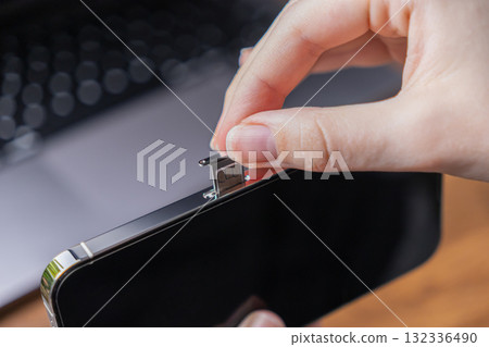Person's hand inserts a tiny SIM card into a modern smartphone, signifying essential mobile network connectivity, telecommunication setup, and global digital communication services 132336490