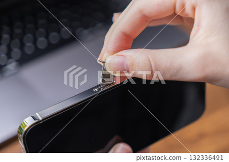 Person's hand carefully inserting a nano SIM card into a modern smartphone using an ejector tool, essential for mobile telecommunications network activation Person's hand carefully inserting a nano SIM card into a modern smartphone using an ejector tool, essential for mobile telecommunications network activation 132336491