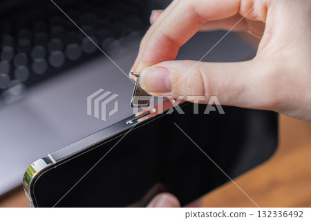 Human hand carefully inserting a dual SIM card tray with microchip into a sleek smartphone for seamless mobile network connectivity and digital communication Human hand carefully inserting a dual SIM card tray with microchip into a sleek smartphone for seamless mobile network connectivity and digital communication 132336492
