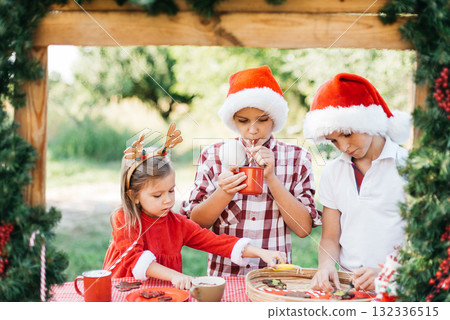Happy children preparing for Christmas. Two boys and girl in santa hat, color gingerbread cookies outside having fun. kids decorate gingerbread man. homemade Christmas cookies. Holidays concept Happy children preparing for Christmas. Two boys and girl in santa hat, color gingerbread cookies outside having fun. kids decorate gingerbread man. homemade Christmas cookies. Holidays concept 132336515