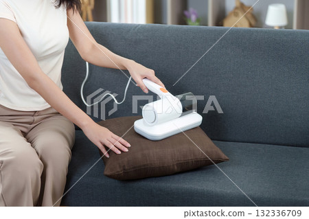Smart Home. Woman using handheld vacuum cleaner on sofa in modern living room. 132336709