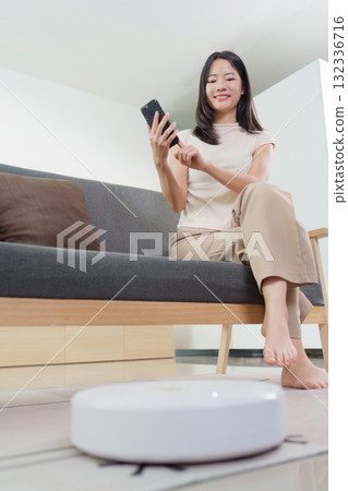 Smart Home: Woman controlling robotic vacuum with smartphone 132336716
