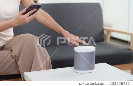 Smart Home. Woman using smartphone to control smart speaker in cozy living room. 132336721