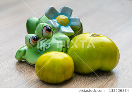 fresh and delicious green tomatoes and a green ceramic frog on a wooden table, closeup 132336884