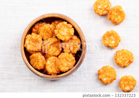 Thai chili rice crackers in a wooden bowl on linen fabric. Hot, sweet and spicy crispies, a snack made of rice, seasoned with chili powder and flavored with soy sauce. Close-up from above, food photo. 132337223