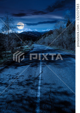 road through mountain landscape of in autumn at night. forest in fall colors under dark sky in full moon light. snow covered peak in the distance. scenic view of rural valley road through mountain landscape of in autumn at night. forest in fall colors under dark sky in full moon light. snow covered peak in the distance. scenic view of rural valley 132337563