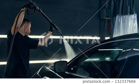 Worker using high pressure washer to clean car windshield in detailing center 132337666
