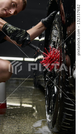 Focused worker cleaning wheel rim with red brush at car detailing center 132337682