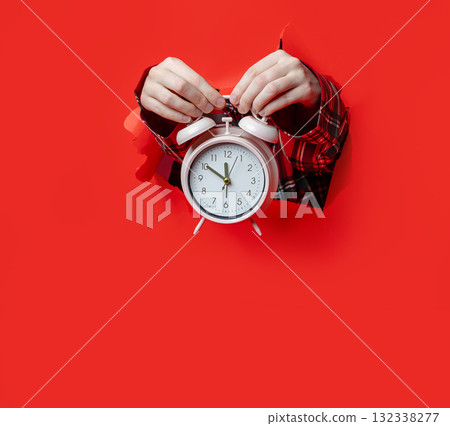 Merry Christmas. A classic white alarm clock is held in hands wearing plaid sleeves 132338277