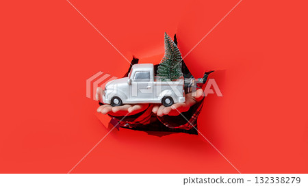 Merry Christmas. Hands in plaid sleeves hold white toy truck carrying mini Christmas tree through torn red background. Merry Christmas. Hands in plaid sleeves hold white toy truck carrying mini Christmas tree through torn red background. 132338279