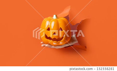 Hand Holding Jack-O'-Lantern. Hand reaches through torn orange paper holding a plastic Jack-O'-Lantern candy bucket. Hand Holding Jack-O'-Lantern. Hand reaches through torn orange paper holding a plastic Jack-O'-Lantern candy bucket. 132338281