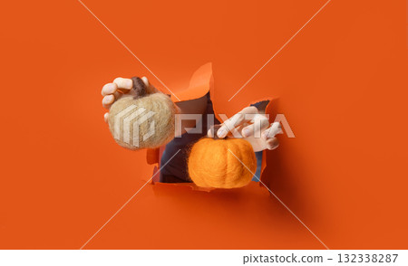 Hand holding soft wool pumpkin with golden stem through torn orange paper background. 132338287
