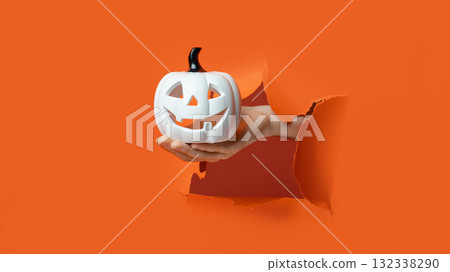 White ceramic Jack-O'-Lantern with a black stem is held through a torn orange background. 132338290