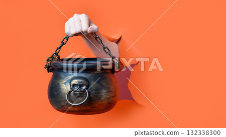 A hand holding a black Halloween cauldron with skull and chain through A hand holding a black Halloween cauldron with skull and chain through 132338300
