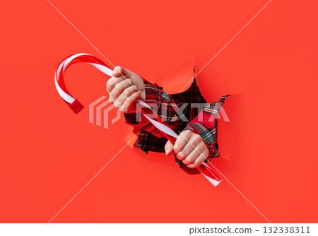 Merry Christmas. Two hands in plaid sleeves hold a large red and white striped candy Merry Christmas. Two hands in plaid sleeves hold a large red and white striped candy 132338311
