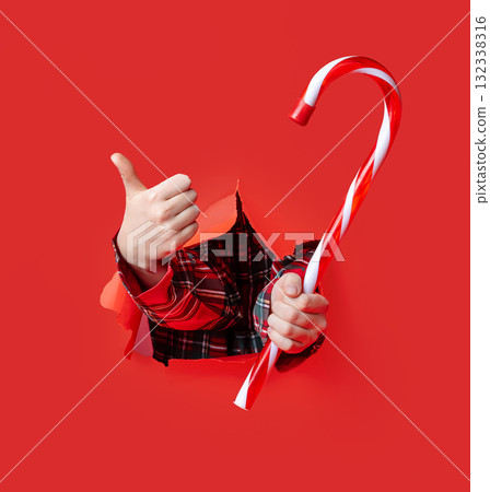 Merry Christmas. Two hands in plaid sleeves hold a large red and white striped candy Merry Christmas. Two hands in plaid sleeves hold a large red and white striped candy 132338316